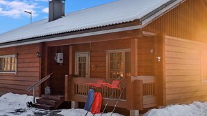 Une cabane en bois avec un porche, une cheminée et un sol recouvert de neige.