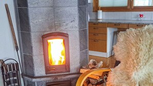 Une cheminée en pierre avec un feu apparent, un porte-bois en bois et un plaid en fourrure.