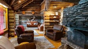 Ein gemütliches Blockhaus-Interieur mit Ledersofas, einem Kamin aus Naturstein und Holzregalen.