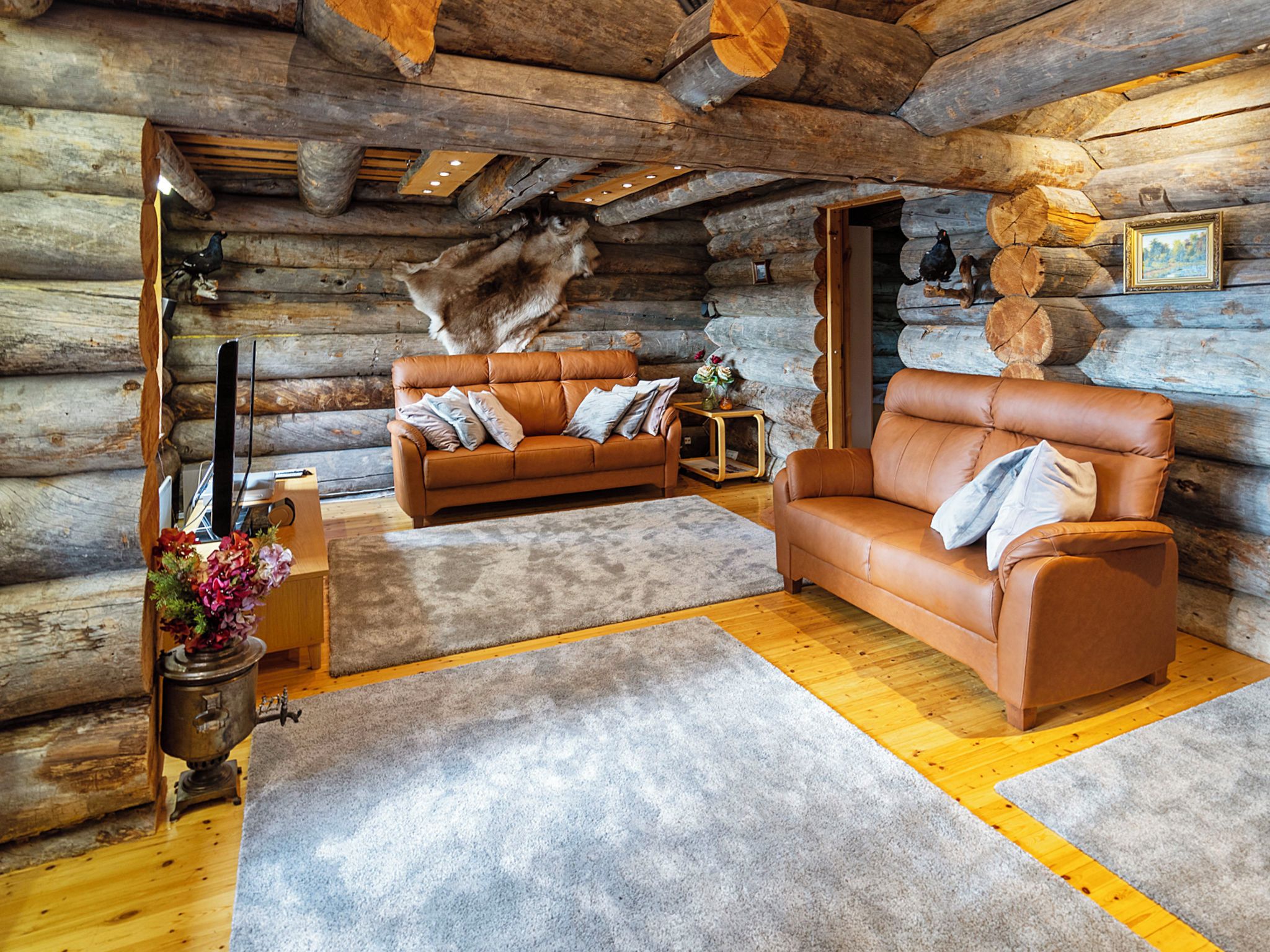 A log cabin interior with two leather sofas, a wooden floor, and a stone wall.