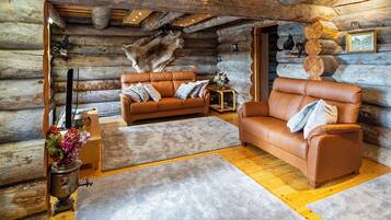 A log cabin interior with two leather sofas, a wooden floor, and a stone wall.