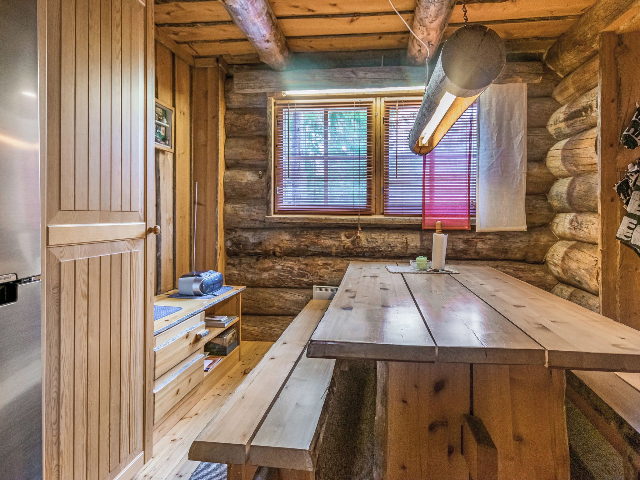 A rustic cabin interior with a wooden table, a built-in shelf, and a window with blinds.