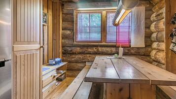 A rustic cabin interior with a wooden table, a built-in shelf, and a window with blinds.