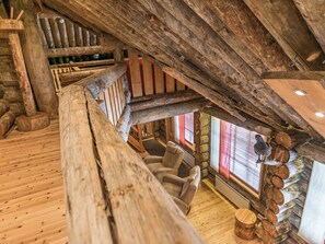 A rustic wooden interior with a loft bedroom, a fireplace, and a cozy seating area.