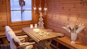 A wooden cabin interior with a dining table, benches, hanging lights, and a decorative wreath on the window. - Alahuone by Interhome (Asikkala)