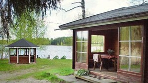 A wooden cabin with a covered porch and large windows, overlooking a lake. - Alahuone by Interhome (Asikkala)