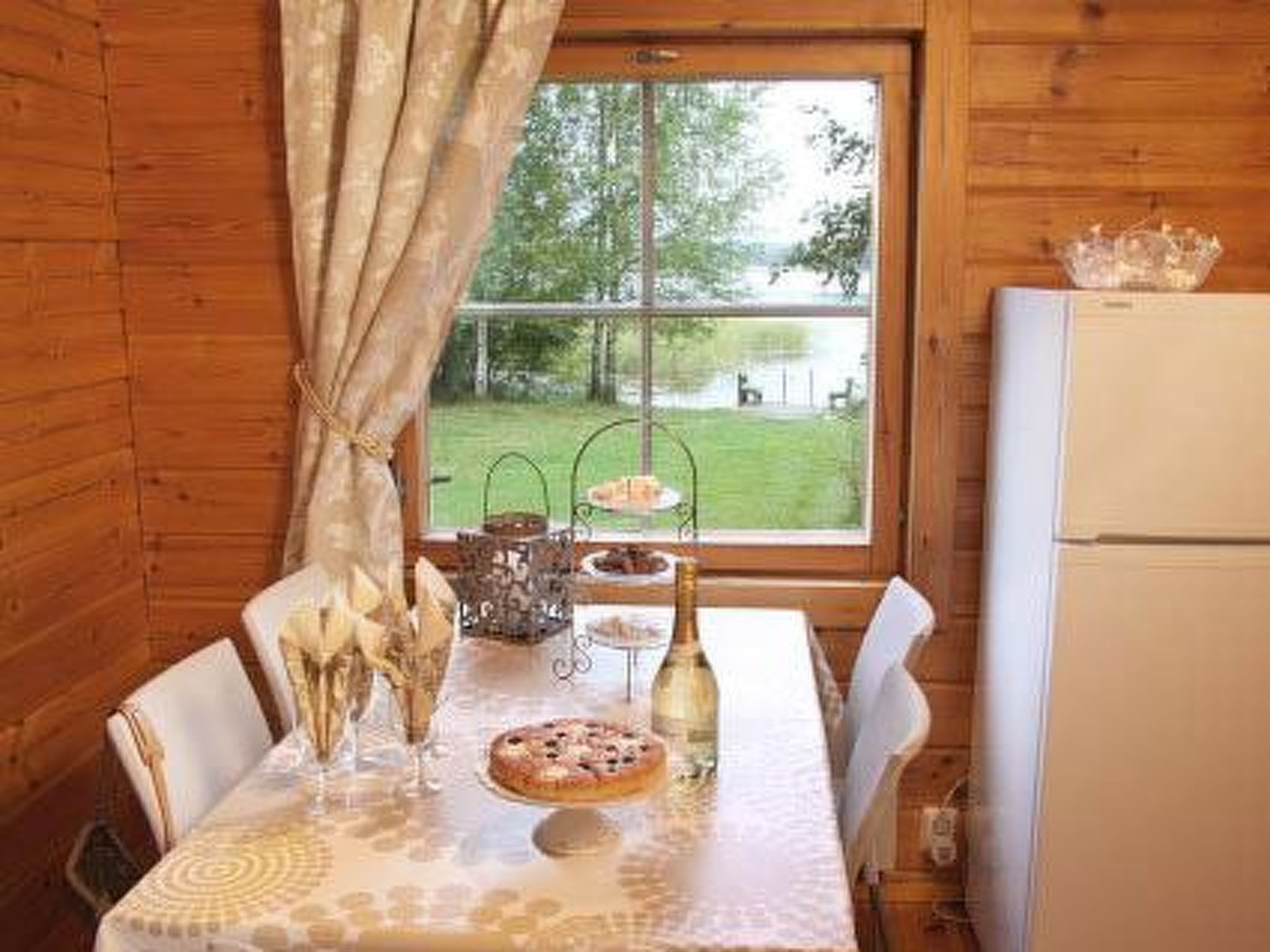 A wooden cabin interior with a dining table set for two, a bottle of wine, and a pizza.