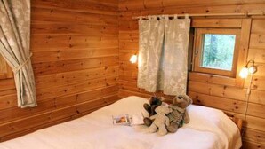 A wooden cabin room with a bed, a window with curtains, and a wall-mounted light fixture. - Alahuone by Interhome (Asikkala)