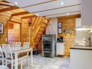 Ein Holzinnenraum mit Esstisch und Stühlen, Kamin und Küchenzeile.