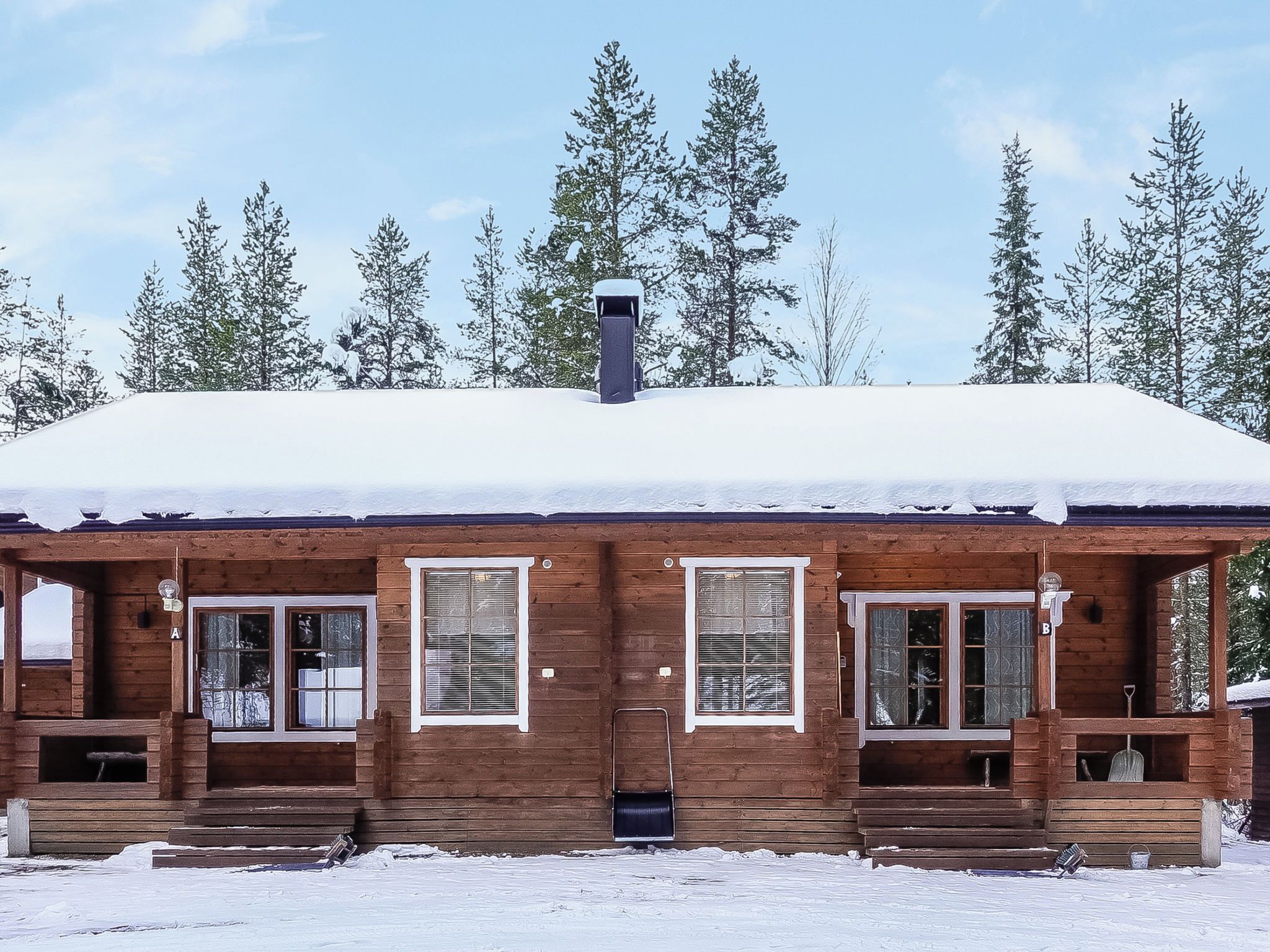 Une cabane en bois avec un toit enneigé, de nombreuses fenêtres et une cheminée.