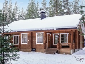 A wooden cabin with multiple windows and a chimney, surrounded by snow-covered ground and trees. - Aslakit b by Interhome (Kittilä)