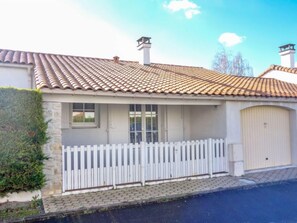 Ein Haus mit einem Ziegeldach, einer Garagentür und einem weißen Zaun.