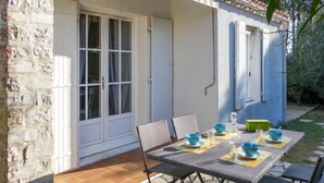Um pátio com mesa posta para refeições, uma parede de pedra e um edifício azul com persianas.