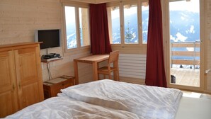 Une chambre à coucher avec un lit, un bureau, une télévision et une fenêtre avec des rideaux.