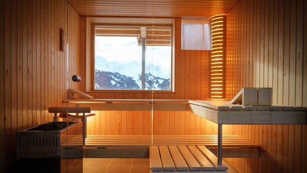 Un sauna aux murs en bois, avec un banc, une table et une fenêtre donnant sur les montagnes.