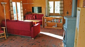 L’intérieur d’un chalet accueillant, avec un canapé rouge, une table en bois, une bibliothèque, une cheminée et un téléviseur.