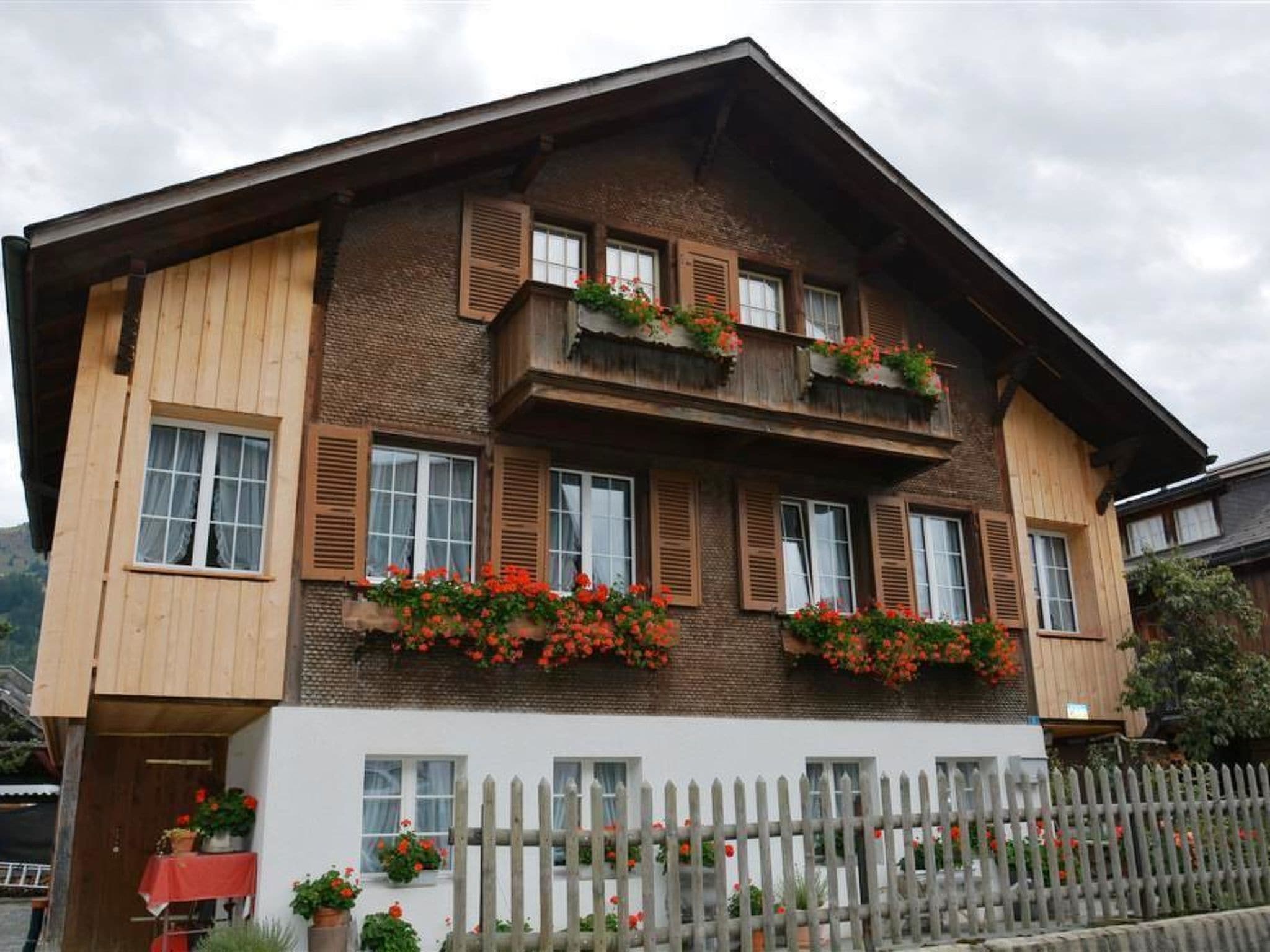 A two-story building with wooden siding and multiple windows, some with shutters. There are flower boxes on the balconies.