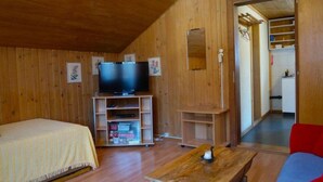 Ett rum med träpanel på väggarna, en säng, en tv på ett stativ, ett litet bord och en röd soffa.