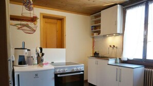 Ett kompakt kök med en spis, ugn och en kaffebryggare. Det finns skåp och ett fönster med gardiner.