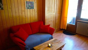 Ett rum med träpanel på väggarna, en röd soffa, ett träbord och ett ljus, samt ett fönster med gardiner.