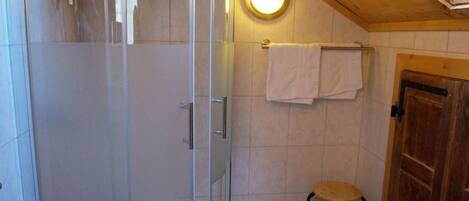 A bathroom with a glass shower enclosure, a wooden door, and a small stool.