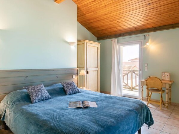 Un dormitorio con cama, armario de madera, una silla y un balcón con barandilla.