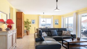 A living room with a sofa, a coffee table, a lamp, a plant, and a view through large windows.