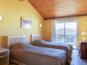 Ein Zimmer mit zwei Betten, einer Holzbalkendecke, einem Fenster mit Blick auf Gebäude und einem kleinen Tisch mit einer Lampe.