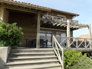 Ein hölzernes Gebäude mit überdachter Veranda, Außenmöbeln und einer Treppe zum Eingang.
