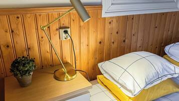 A wooden-paneled room with a bedside table, a lamp, a potted plant, and a bed with a white and yellow bedding.
