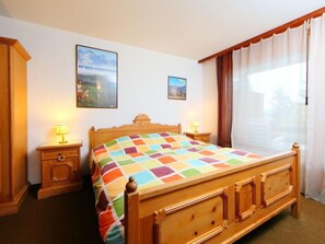 Une chambre à coucher avec un lit en bois, deux tables de chevet avec des lampes, une grande fenêtre avec des rideaux et deux tableaux encadrés accrochés au mur.