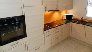 A modern kitchen with light wood cabinets, a black stove, a microwave, and a sink.