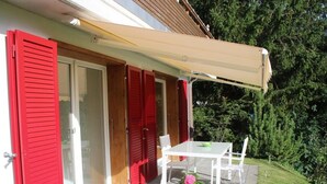 A patio with a table and chairs, a red door, and a white awning.