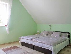 Ein Schlafzimmer mit Bett, Nachttisch, Lampe und einem Fenster mit Vorhang.