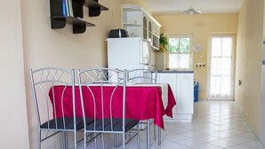 A dining area with a table covered by a red tablecloth and metal chairs, a white refrigerator, and a kitchen area with cabinets and a window. - Vacation home Welle by Interhome (Balatonmariafurdo)