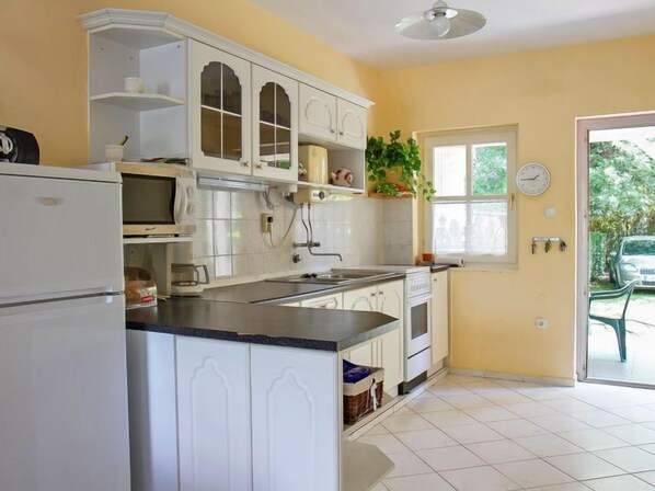 A kitchen with white cabinets, a microwave, and a sink. There is a window with a view of greenery outside. - Vacation home Welle by Interhome (Balatonmariafurdo)