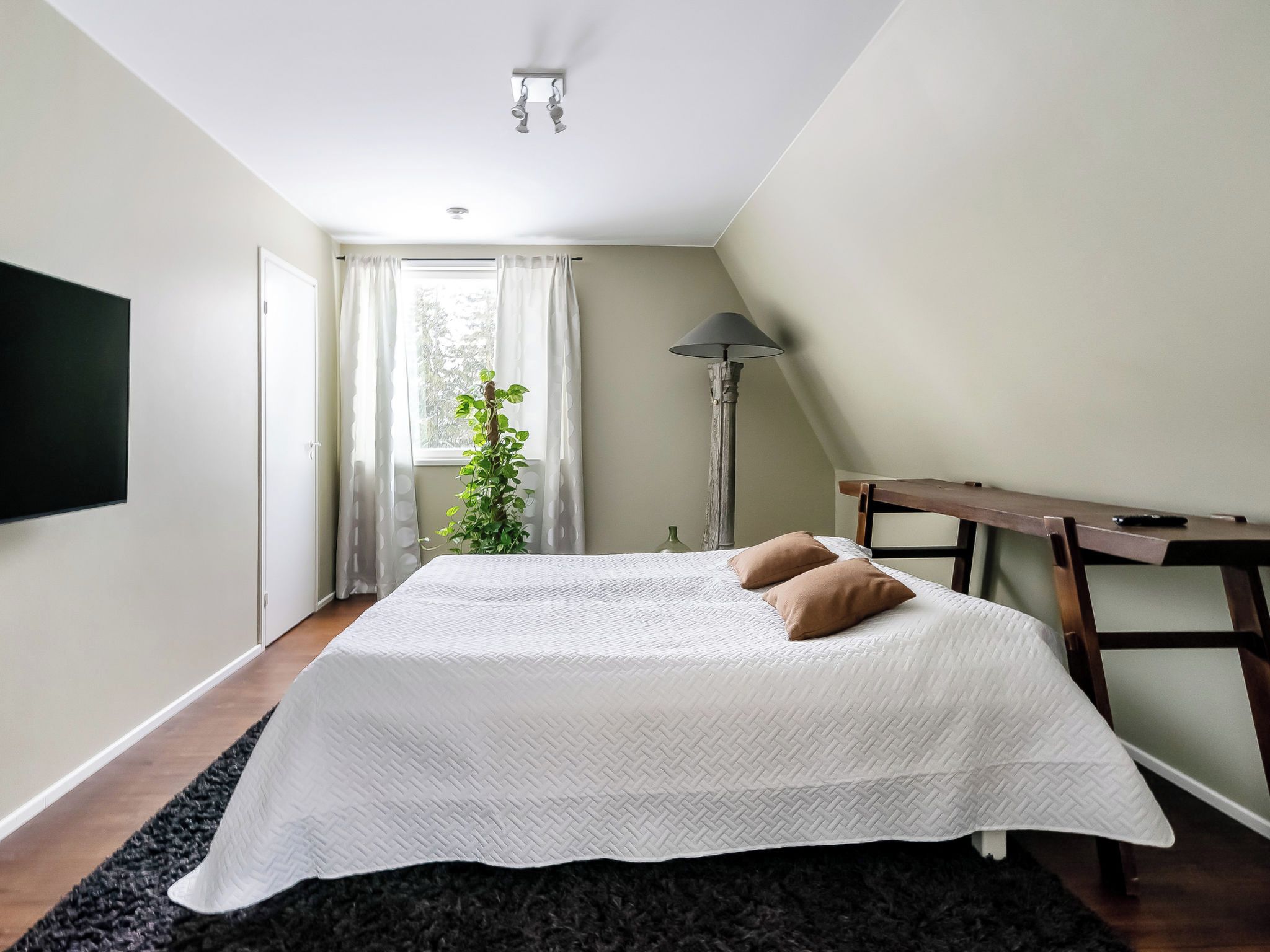 Ein Schlafzimmer mit einem großen Bett, einem Nachttisch, einer Lampe und einem Fenster mit Vorhängen.