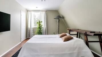 Ein Schlafzimmer mit einem großen Bett, einem Nachttisch, einer Lampe und einem Fenster mit Vorhängen.