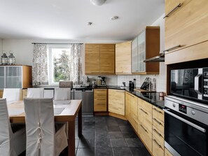 Une cuisine moderne avec des meubles en bois, un four encastré et un coin repas comprenant une table et des chaises.