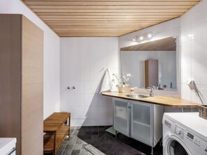 Un baño moderno con techo de madera, un lavamanos empotrado, un espejo, una lavadora y un banco.