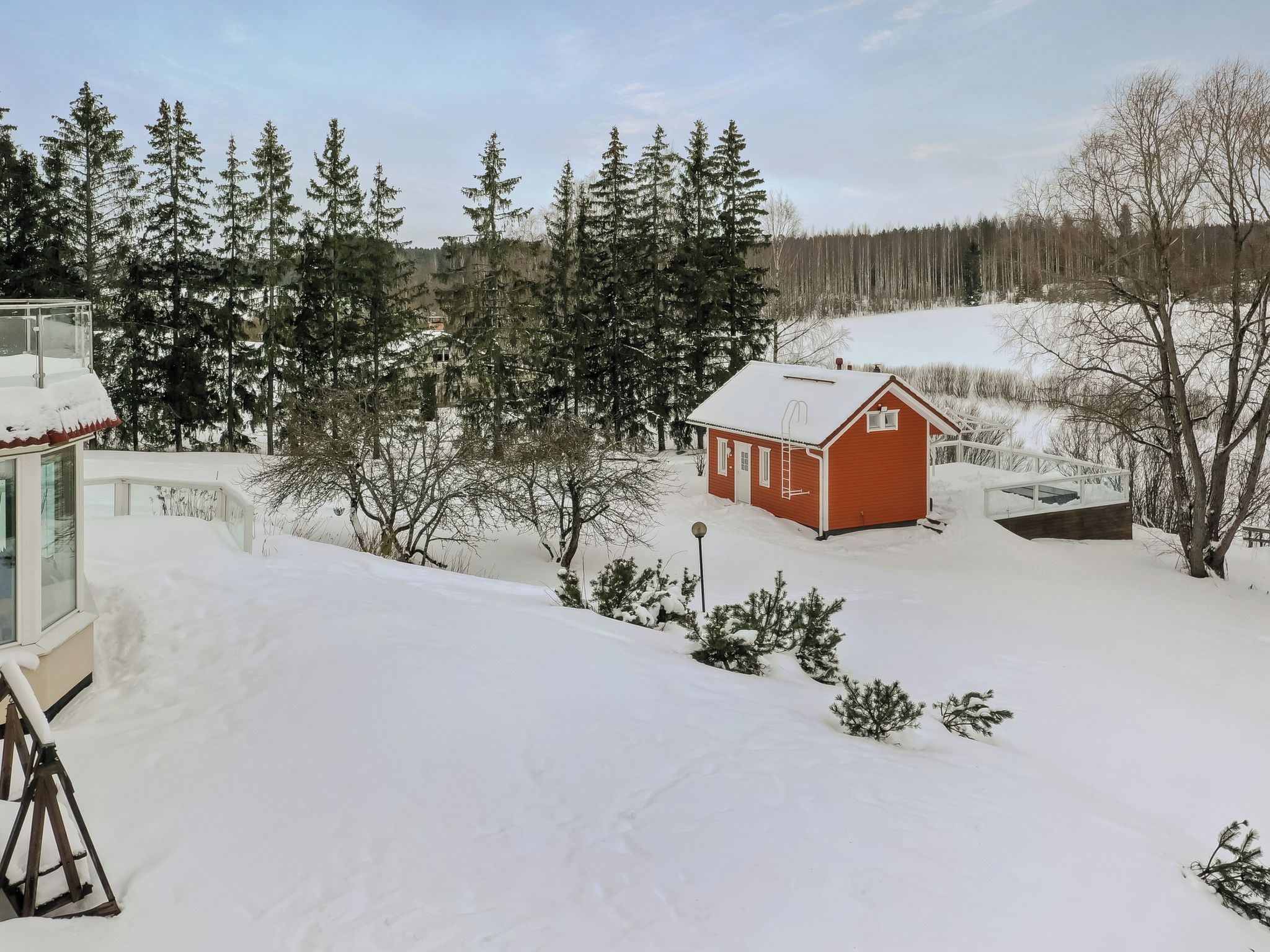 A snow-covered landscape with a small red cabin and a large building with a glass facade.
