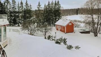A snow-covered landscape with a small red cabin and a large building with a glass facade.