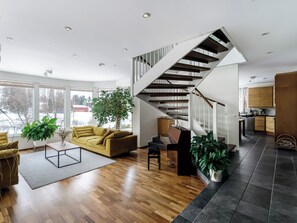 Una sala de estar moderna con escaleras, suelo de madera y ventanas amplias.