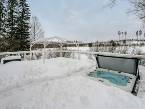 Zona exterior nevada con jacuzzi y una estructura de madera al fondo.