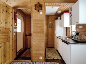 Un intérieur en bois avec un coin cuisine comprenant des meubles blancs, un évier et une machine à café.