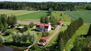 Suuri talo, jossa on punainen katto, ja sen ympärillä on vihreitä peltoja ja joki.