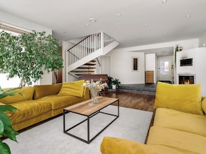 Una sala moderna con un sofá amarillo, una mesa de centro de madera y una escalera que sube a un nivel superior.