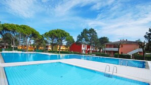 Ein Swimmingpool mit gefliesten Rändern und glasklar blauem Wasser, umgeben von Bäumen und Gebäuden, mit blauem Himmel darüber.
