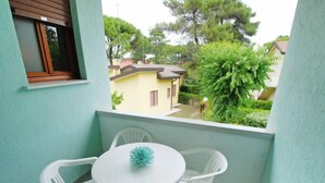 Ein Balkon mit weißem Tisch und Stühlen, einem Blumentopf und Blick auf eine Wohngegend mit Häusern und Bäumen.