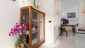 Una habitación con un armario de madera, una mesa de comedor con sillas y un jarrón de flores moradas.